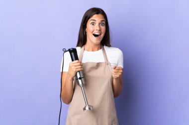 Brazilian woman using hand blender isolated on purple background celebrating a victory in winner position