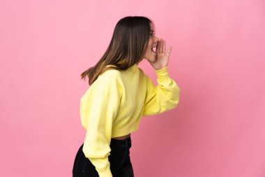 Teenager girl isolated on pink background shouting with mouth wide open to the side