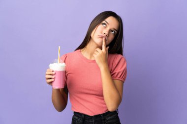 Teenager girl holding a strawberry milkshake having doubts while looking up