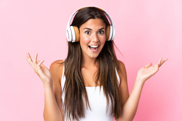 Young brazilian girl isolated on pink background surprised and listening music