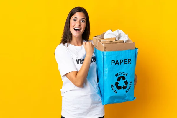 勝利を祝う黄色の背景に隔離されたリサイクル紙の袋を持っている若いブラジル人の女の子 — ストック写真