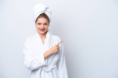 Beyaz arka planda izole edilmiş bornozlu genç Rus kız bir ürün sunmak için kenarı işaret ediyor.