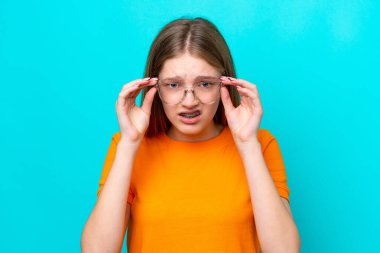 Genç Rus kız mavi arka planda gözlüklü ve sinirli bir ifadeyle izole edilmiş.