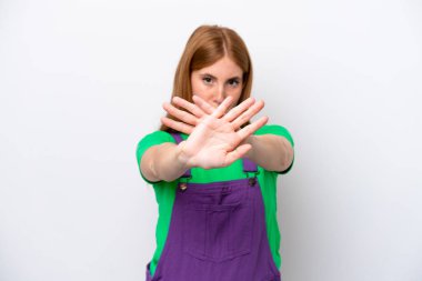 Beyaz arka planda izole edilmiş genç kızıl saçlı kadın bir hareketi durdurmak için elleriyle hareket yapıyor.