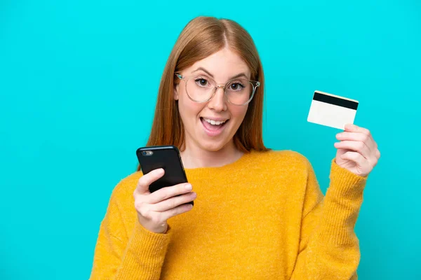 Jonge Roodharige Vrouw Geïsoleerd Blauwe Achtergrond Kopen Met Mobiele Telefoon — Stockfoto