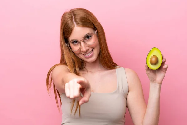 Junge Rothaarige Frau Hält Eine Avocado Isoliert Auf Rosa Hintergrund — Stockfoto