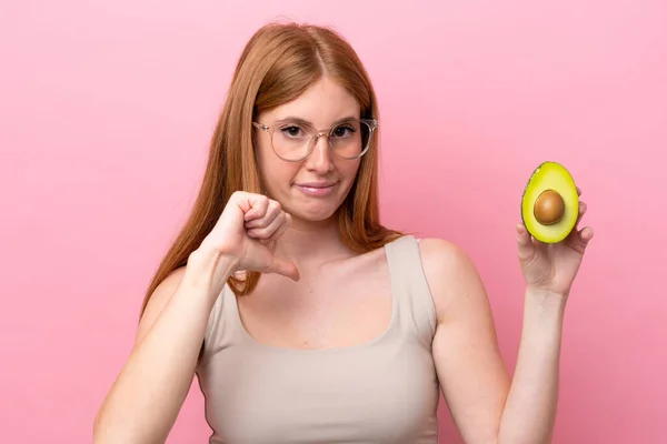 Young Redhead Woman Holding Avocado Isolated Pink Background Showing Thumb — Stock Photo, Image