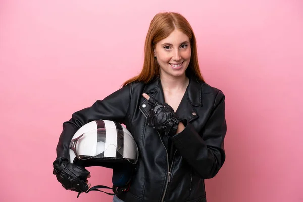 Young redhead woman with a motorcycle helmet isolated on pink background pointing to the side to present a product