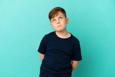 Küçük kızıl çocuk mavi arka planda izole edilmiş ve yukarı bakıyor.