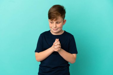 Küçük kızıl saçlı çocuk mavi arka planda yalnız gülüyor.