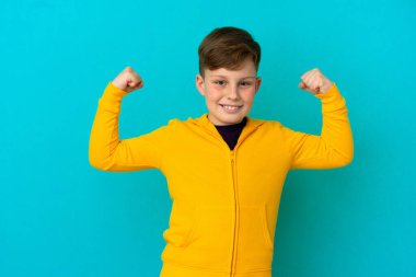 Mavi arka planda izole edilmiş küçük kızıl çocuk güçlü bir jest yapıyor.