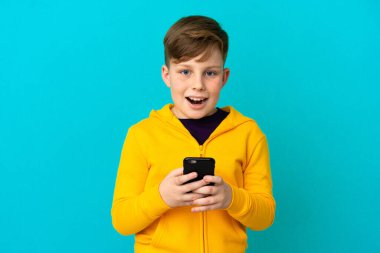 Mavi arka planda izole edilmiş küçük kızıl çocuk şaşırdı ve bir mesaj gönderiyor.