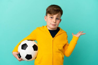 Mavi arka planda futbol oynayan kızıl saçlı çocuk ellerini kaldırırken şüphe duyuyor.