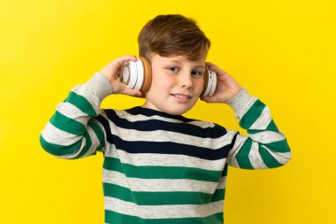 Sarı arka planda izole edilmiş küçük kızıl çocuk müzik dinliyor.