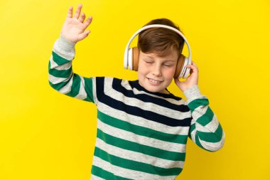 Sarı arka planda izole edilmiş küçük kızıl çocuk müzik ve dans dinliyor.