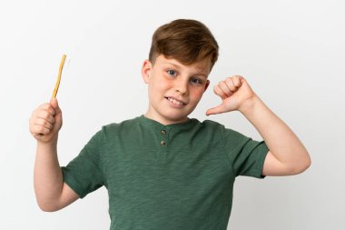 Beyaz arka planda izole edilmiş diş fırçası tutan küçük kızıl çocuk gururlu ve kendini beğenmiş.