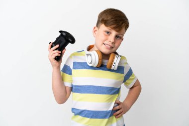 Küçük kızıl saçlı çocuk beyaz arka planda izole edilmiş bir oyun tahtası tutuyor. Kolları kalçasında ve gülümsüyor.