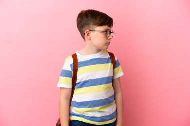 Küçük kızıl saçlı beyaz çocuk pembe arka planda izole edilmiş, yan tarafa bakıyor.