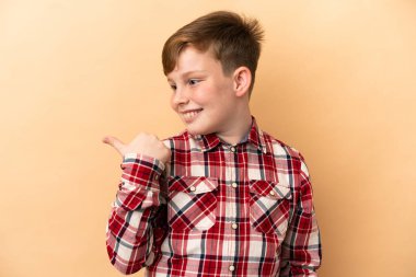 Bej arka planda izole edilmiş küçük kızıl saçlı çocuk.