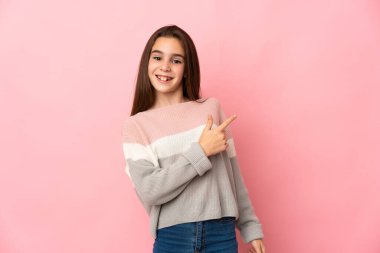 Pembe arka planda izole edilmiş küçük kız şaşırmış ve işaret ediyor.