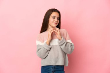 Küçük kız pembe arka planda bir şeyler planlıyor.