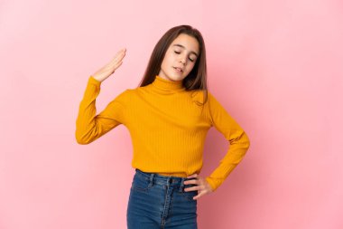 Küçük kız pembe arka planda yalnız, yorgun ve hasta bir ifadeyle.