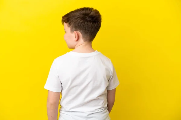 後ろの黄色の背景に隔離された小さな赤毛の少年と見ている側 — ストック写真
