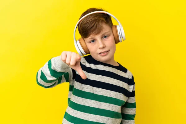 被黄色背景隔离的红头发小男孩听着音乐 — 图库照片