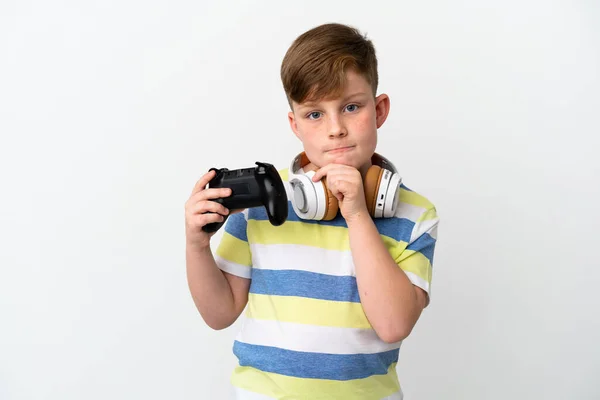 一个红头发的小男孩拿着一个白色背景的游戏垫 有着怀疑和思考 — 图库照片