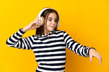 Sarı arka planda izole edilmiş küçük kız müzik ve dans dinliyor.