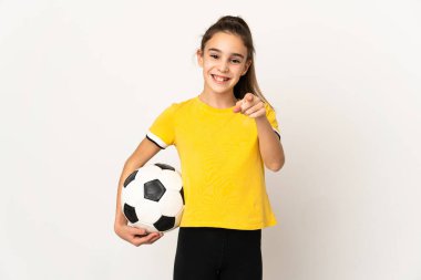 Beyaz arka planda izole edilmiş küçük futbolcu kız şaşırmış ve ön tarafı işaret ediyor.