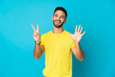 Mavi arka planda izole edilmiş genç beyaz adam yediyi parmaklarıyla sayıyor