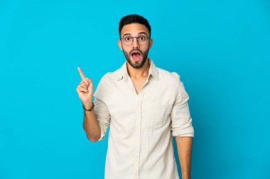 Kafkasyalı genç adam mavi arka planda izole edilmiş bir şekilde parmağını kaldırarak çözümü anlamaya çalışıyor.