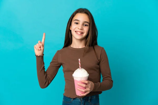 女の子ともにイチゴミルクセーキ隔離上の青背景ショーと持ち上げる指で最高のサイン — ストック写真