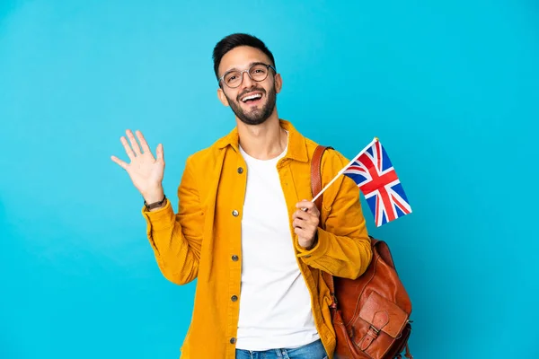 黄色の背景に孤立した英国の旗を手で幸せな表情で塩漬けに保持している若い白人男性 — ストック写真