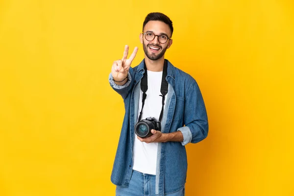 Junges Fotografenmädchen Auf Gelbem Hintergrund Lächelt Und Zeigt Siegeszeichen — Stockfoto
