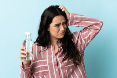 Mavi arka planda su izole edilmiş genç bir kadının şüpheleri ve kafası karışmış bir yüz ifadesi var.