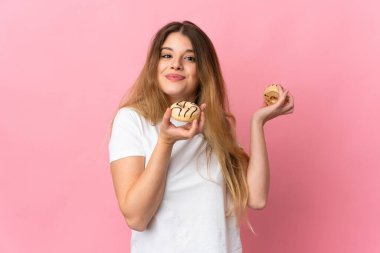 Pembe arka planda izole edilmiş genç sarışın kadın elinde donut tutuyor.