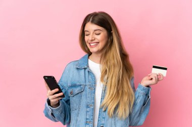 Genç sarışın kadın mavi arka planda izole edilmiş. Kredi kartıyla cep telefonuyla alışveriş yapıyor.