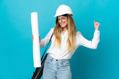 Kasklı ve elinde mavi arka planda izole edilmiş planları olan genç bir mimar kadın zaferi kutluyor.