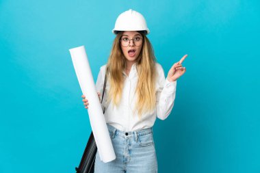 Miğferli ve elinde mavi arka planda izole edilmiş planları olan genç mimar kadın çözümü fark ederken parmağını kaldırmayı amaçlıyor.