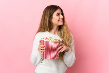 Pembe arka planda izole edilmiş genç sarışın kadın elinde koca bir kova patlamış mısır tutuyor.