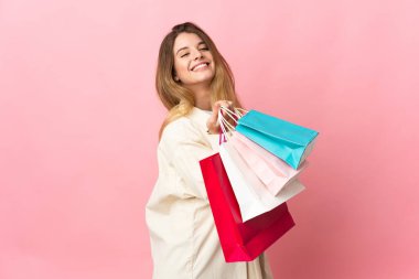 Alışveriş çantalı genç bir kadın pembe arka planda izole edilmiş alışveriş torbaları tutuyor ve gülümsüyor.