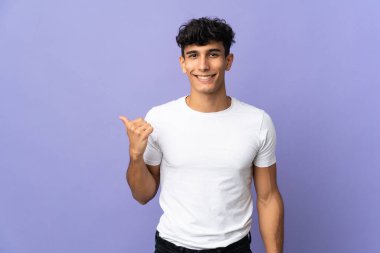 Arka planda izole edilmiş genç Arjantinli bir adam bir ürün sunmak için kenarı işaret ediyor