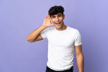 Arjantinli genç adam arka planda izole edilmiş bir şekilde bir şeyler dinlerken elini kulağına koydu.