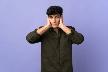 Arjantinli genç adam arka planda izole edilmiş hayal kırıklığına uğramış ve kulaklarını kapatmış.