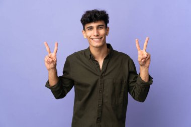 Arjantinli genç adam arka planda iki eliyle zafer işareti gösteriyor.