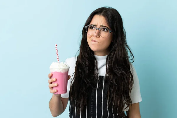 Ung Kvinna Med Jordgubbsmjölkshake Isolerad Blå Bakgrund Med Tvivel Och — Stockfoto