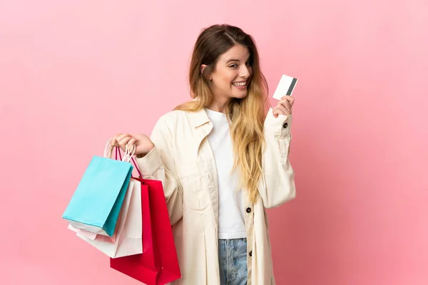 ショッピングバッグとクレジットカードを持つピンクの背景に隔離されたショッピングバッグを持つ若い女性 — ストック写真