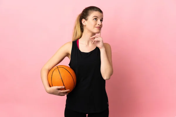 Молодая Блондинка Играющая Баскетбол Розовом Фоне Сомневается Глядя Вверх — стоковое фото